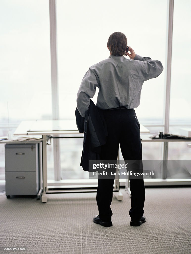 Executive talking on cell phone, looking out office window, rear view