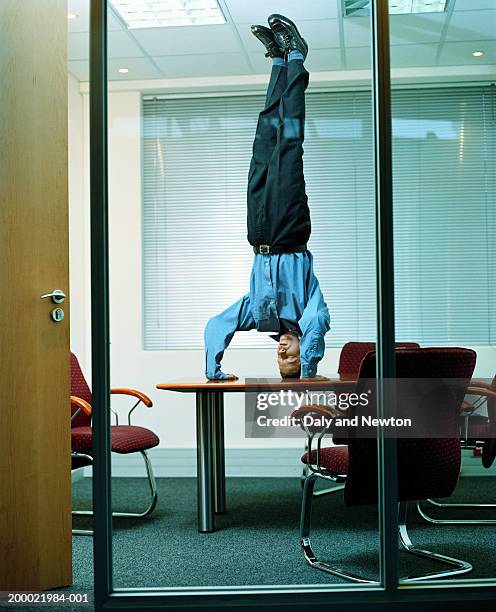 young businessman doing headstand on office table - al revés posición descriptiva fotografías e imágenes de stock