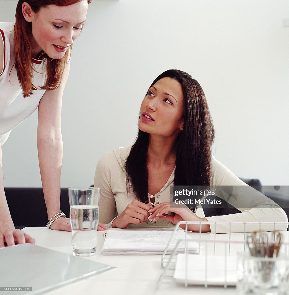 Two women in discussion, one sitting at desk