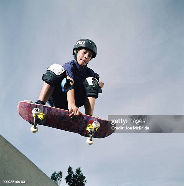 boy (9-11) performing mid-air jump on skateboard, low angle view - boy skatepark stock-fotos und bilder