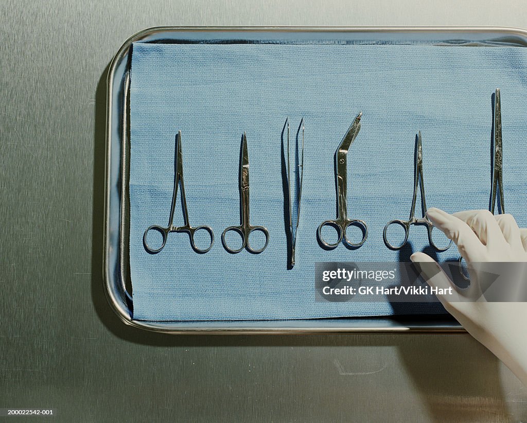 Gloved hand reaching for surgical scissors on metal tray