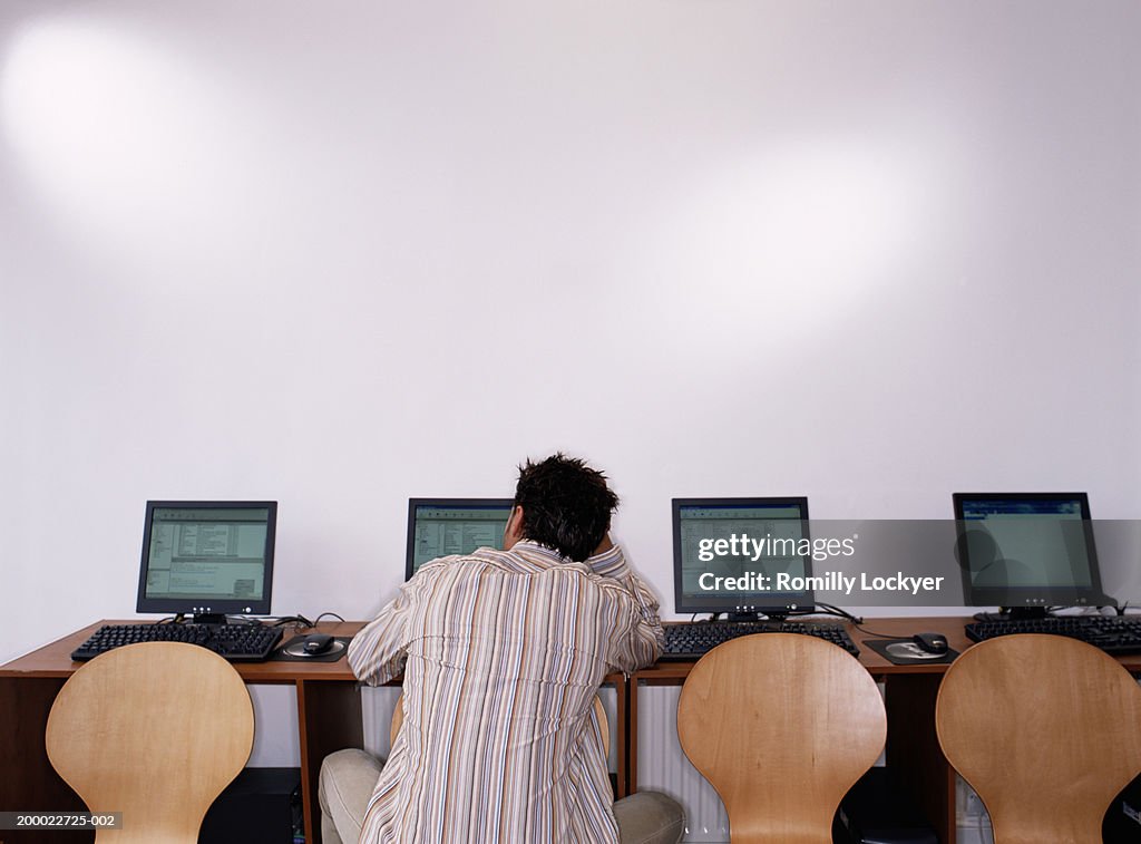 Man using computer in internet cafe, rear view