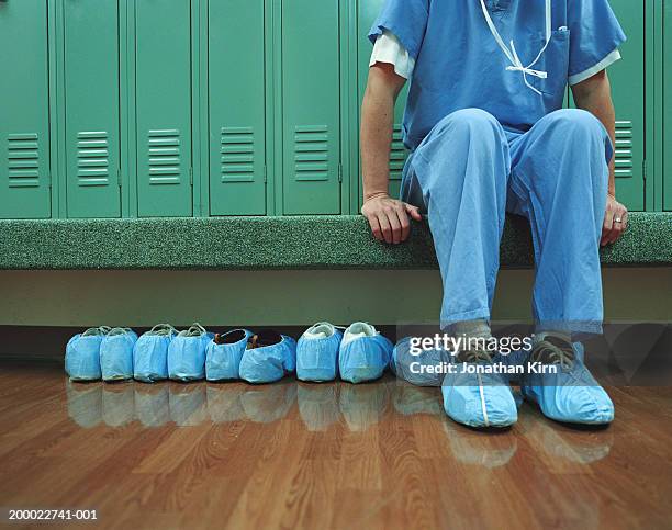 medical worker wearing overshoes in locker room, low section - vestimenta de hospital fotografías e imágenes de stock