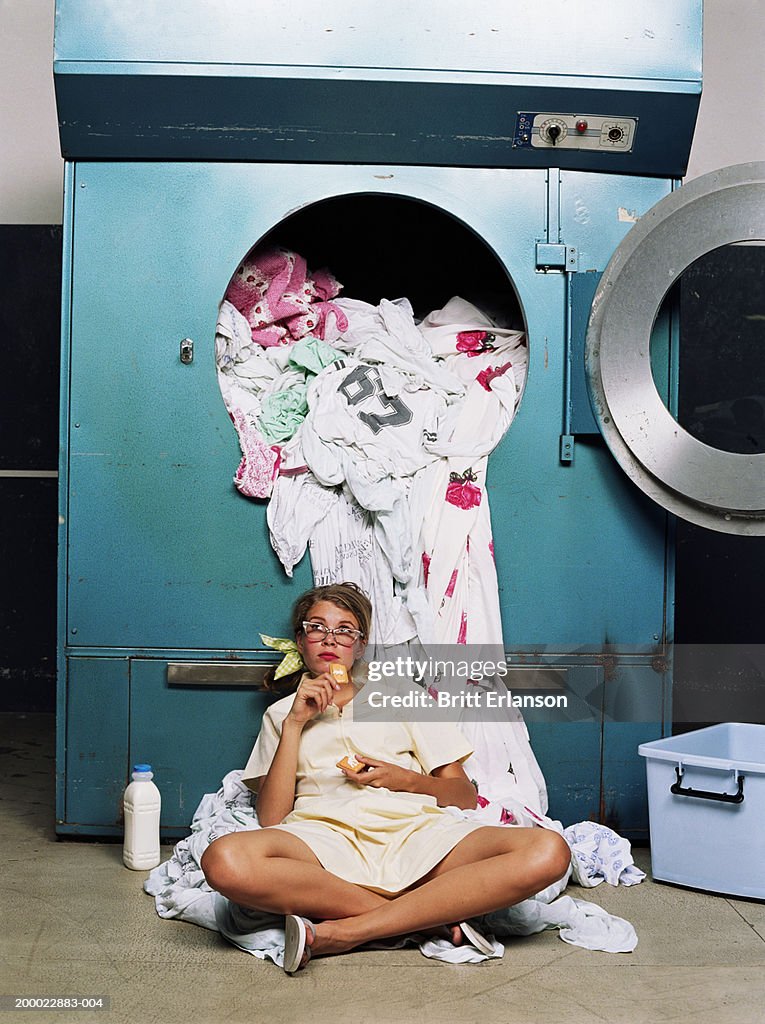 Teenage girl (16-18) taking break beside industrial washing machine
