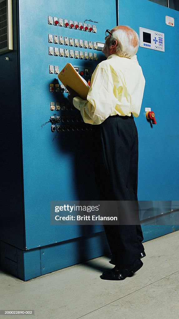 Elderly man with clipboard examining control panel