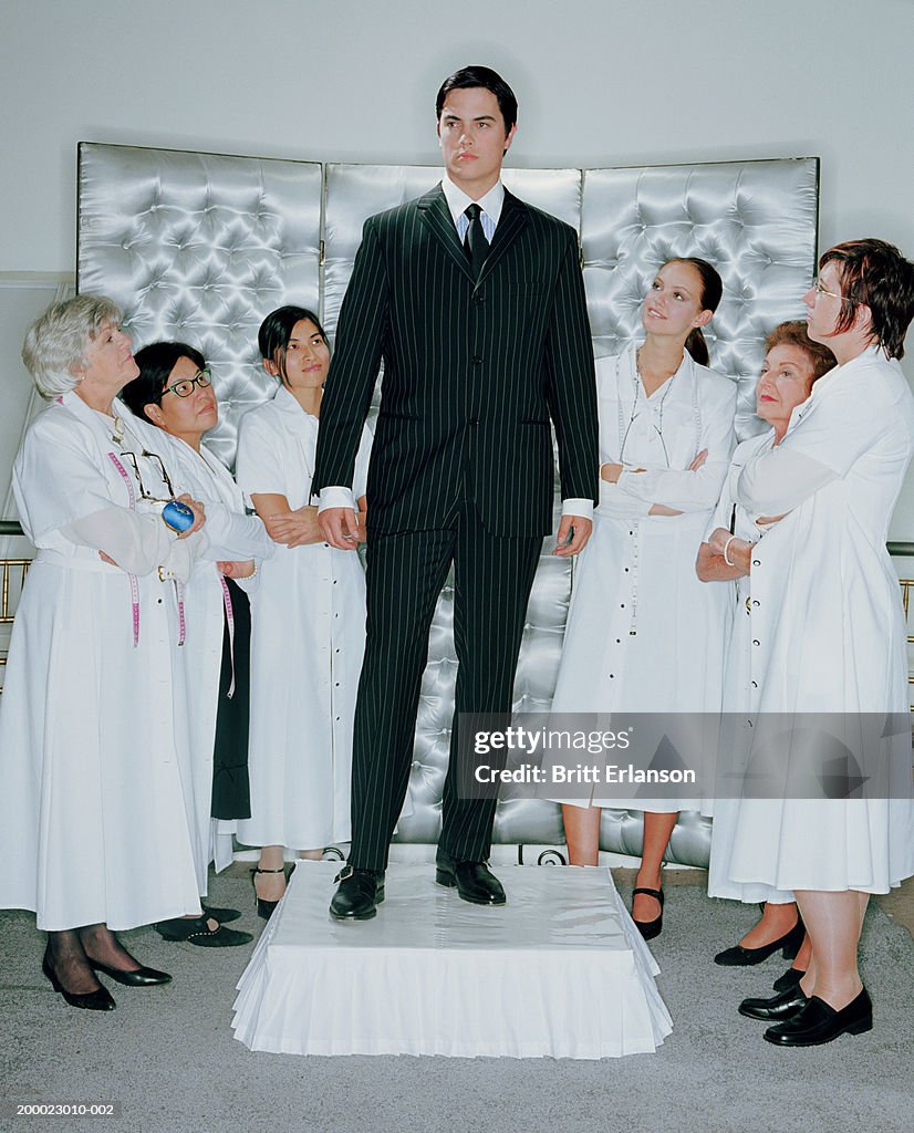 Young businessman on plinth, surrounded by group of women