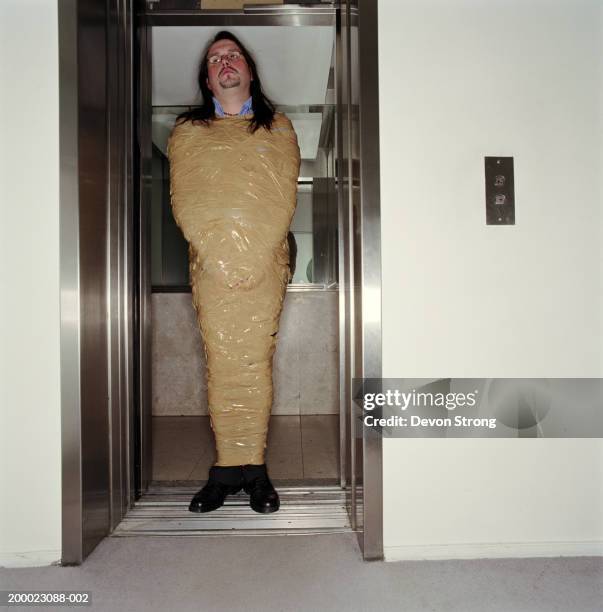 man wrapped in packing tape standing in lift - elevator trapped stock pictures, royalty-free photos & images