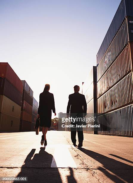 two executives walking by stacks of cargo containers, rear view - 2 businessmen in silhouette stock pictures, royalty-free photos & images
