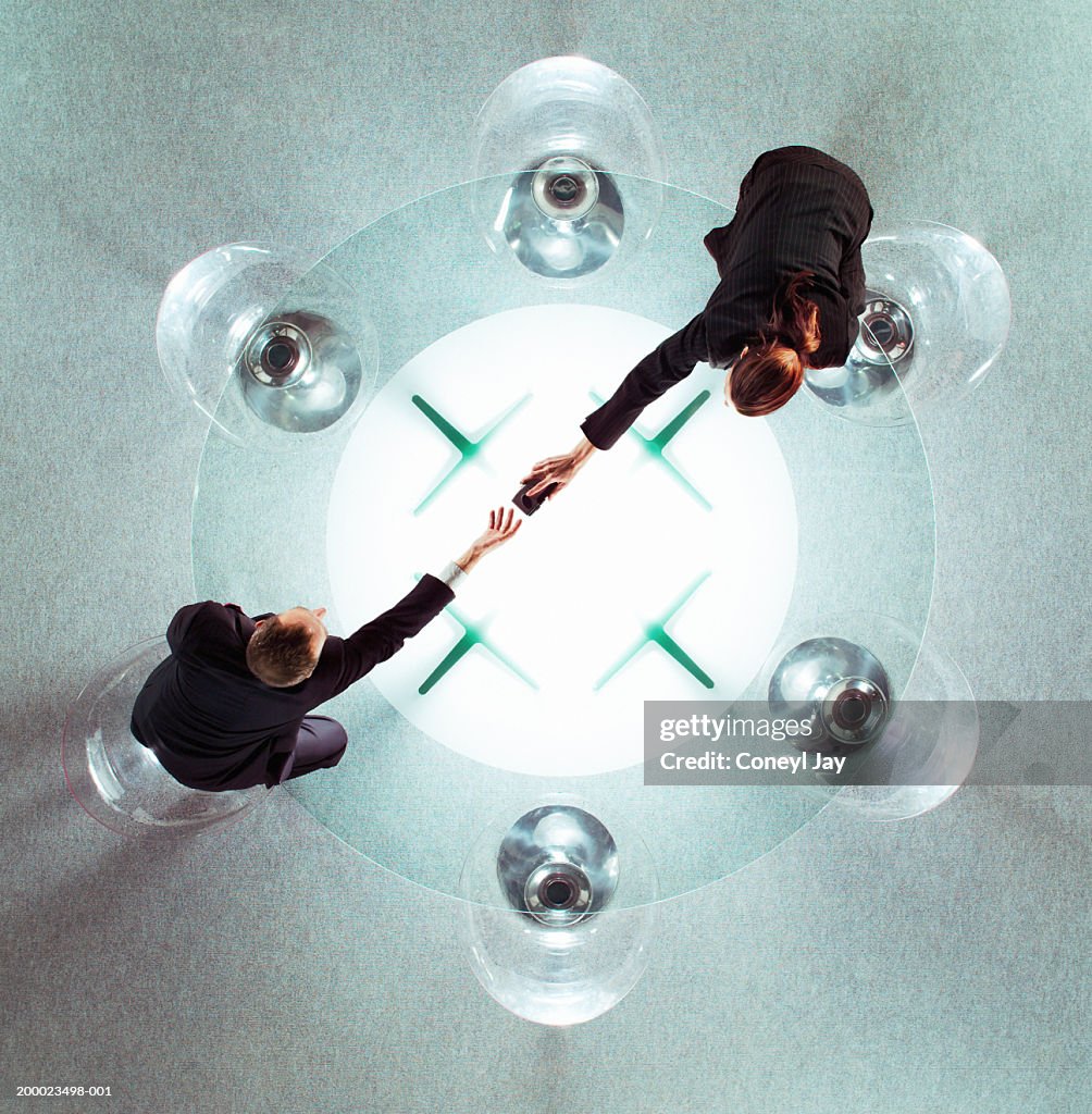 Two business people reaching across glass table, overhead view