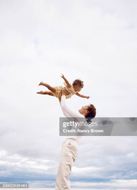 mother lifting baby girl (12-15 months) overhead at beach, low angle - 飛行機のまね ストックフォトと画像