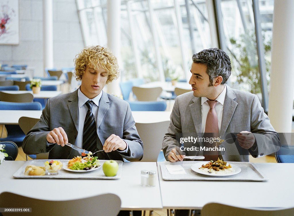 Two male business colleagues in canteen having lunch