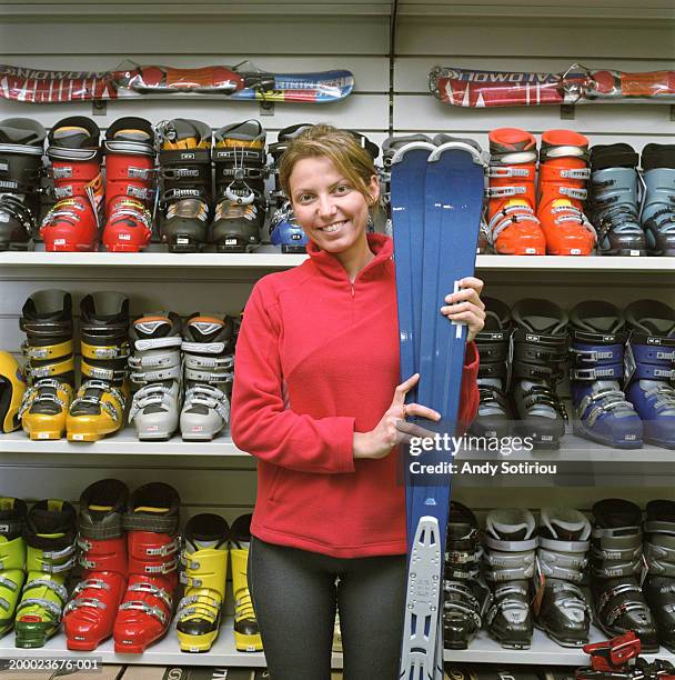 woman beside ski boot display in sports shop, holding skis, portrait - skischoen stockfoto's en -beelden