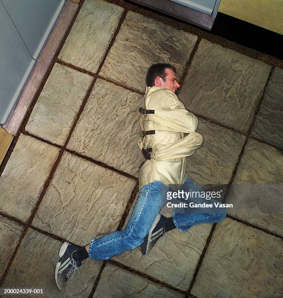 man wearing straitjacket struggling on patio, elevated view - straight jacket stock-fotos und bilder
