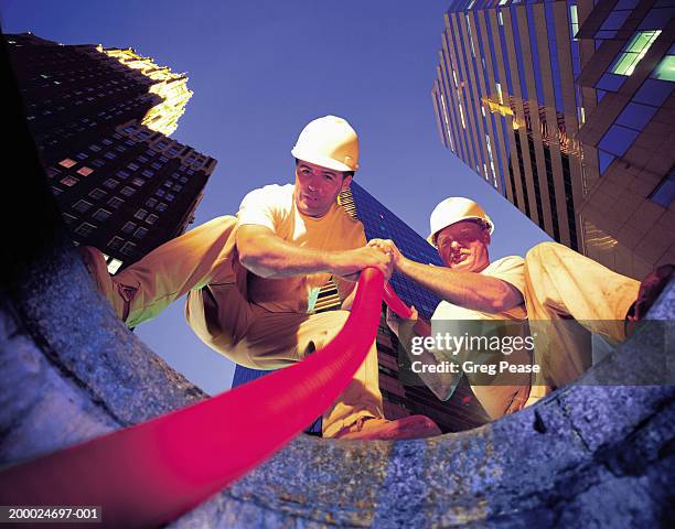 two workmen lowering cable into manhole (digital composite) - cable installation stock pictures, royalty-free photos & images