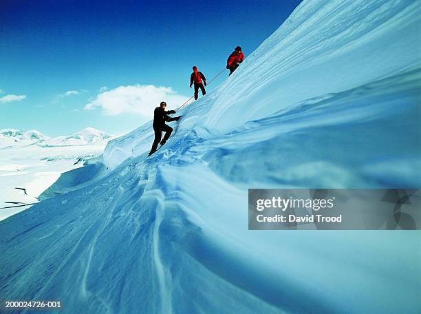 three men climbing icy cliff using rope - david cliff stock-fotos und bilder