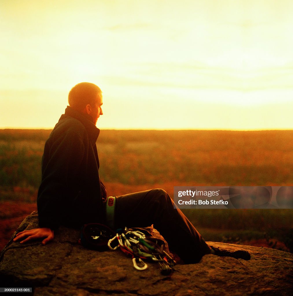 Male rock climber sitting on edge of cliff