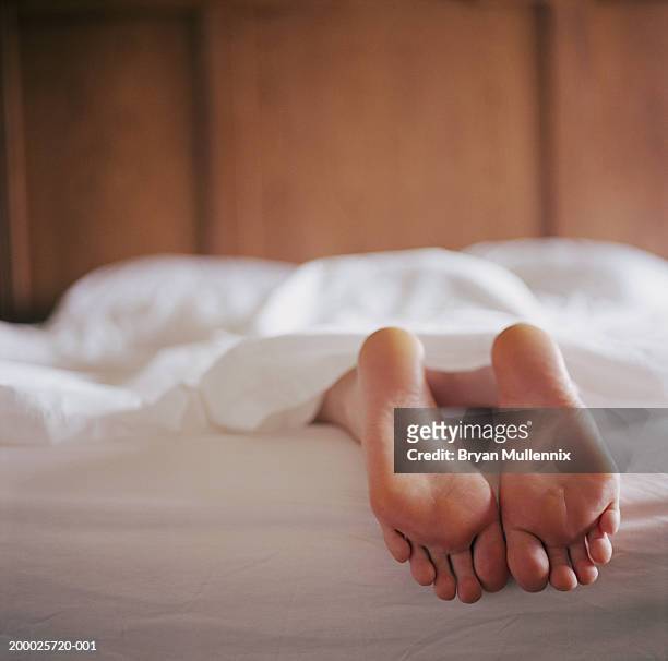 woman lying in bed under sheet (focus on feet) - woman lying on stomach with feet up stock pictures, royalty-free photos & images