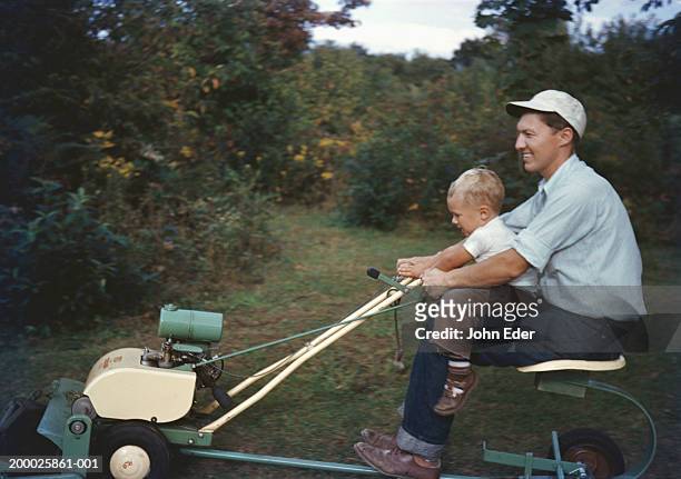 father driving riding lawnmower with son (21-24 months)  on lap - 1950s father stock pictures, royalty-free photos & images