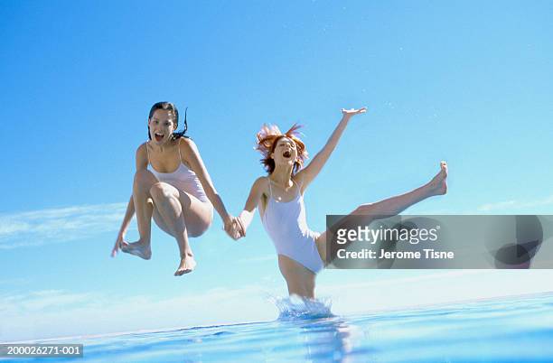 two young women jumping in water - traje de baño de una pieza fotografías e imágenes de stock