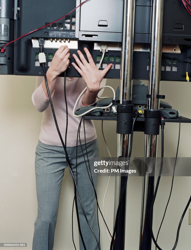 Woman reaching under teleconference screen to connect cable