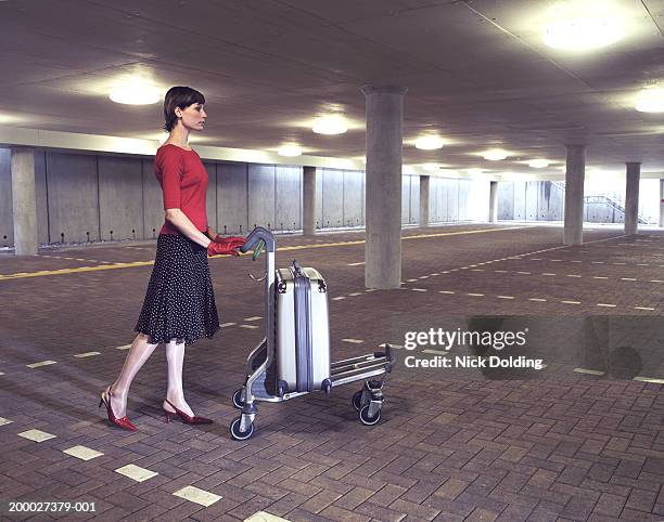 young woman pushing luggage trolley through empty car park - business frau profil kurze haare stock-fotos und bilder