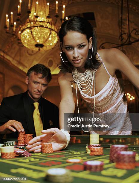 young woman pushing gambling chips on casino table, portrait - roulette photos et images de collection