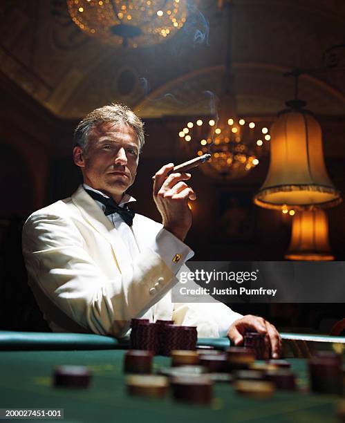 man wearing dinner jacket smoking cigar in casino, portrait - smoking cigar fotografías e imágenes de stock