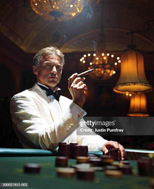 man wearing dinner jacket smoking cigar in casino, portrait - tuxedo foto e immagini stock