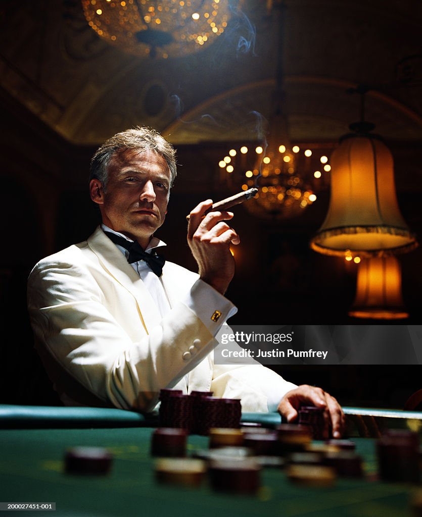 Man wearing dinner jacket smoking cigar in casino, portrait