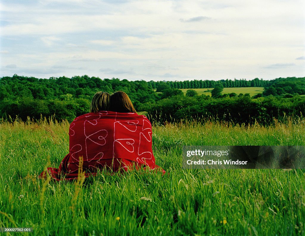 Young couple wrapped in blanket in field, rear view