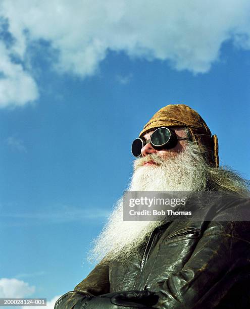 mature bearded man wearing leather jacket and goggles, outdoors - motociclista fotografías e imágenes de stock