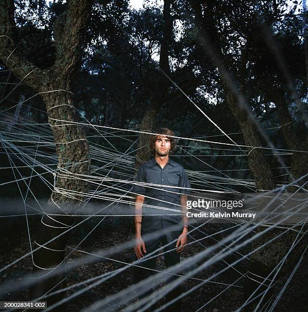 young man standing amongst trees entwined with string, portrait - exclusion concept stock pictures, royalty-free photos & images