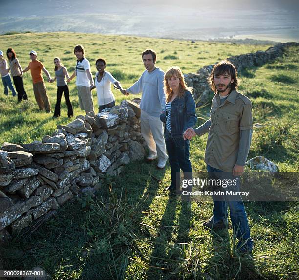 row of people holding hands over dry stone wall, portrait - symbols of peace stock pictures, royalty-free photos & images