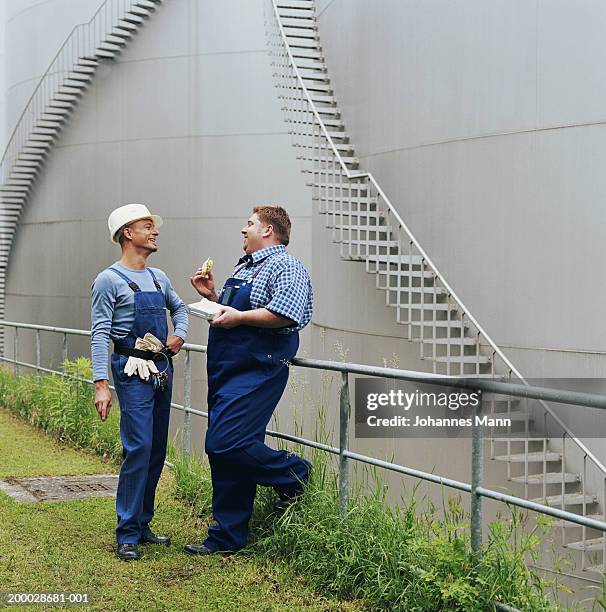 two workmen laughing outside power station, one eating snack - blue jumpsuit stock pictures, royalty-free photos & images