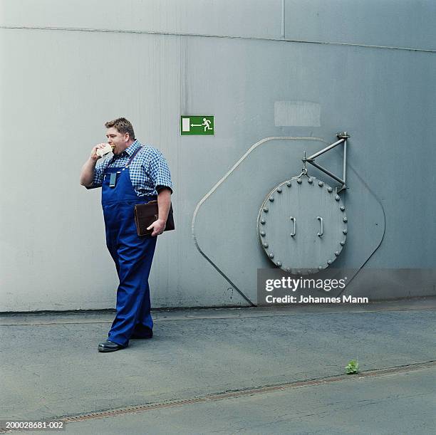 workman walking outside power station, eating snack - fat man overalls stock pictures, royalty-free photos & images