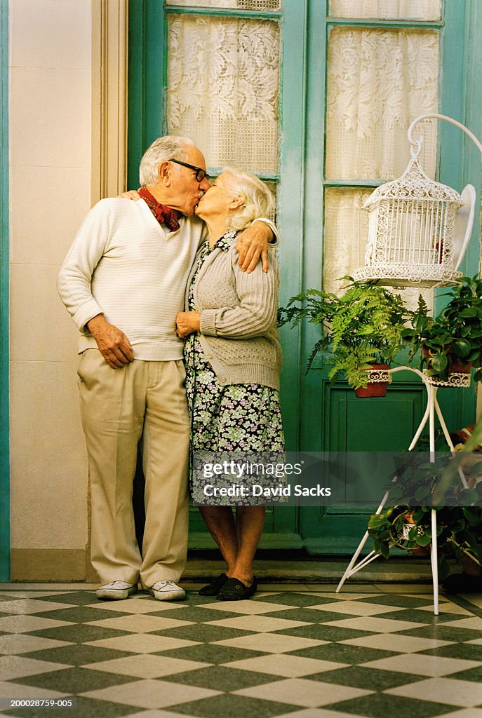 Elderly couple kissing outside house