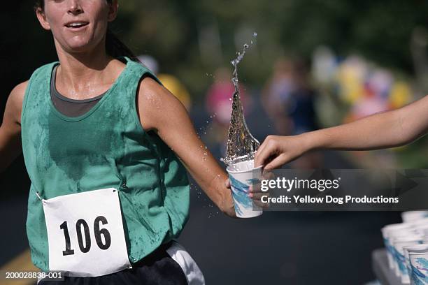 woman running road race, grabbing cup of water, mid-section - race day stockfoto's en -beelden