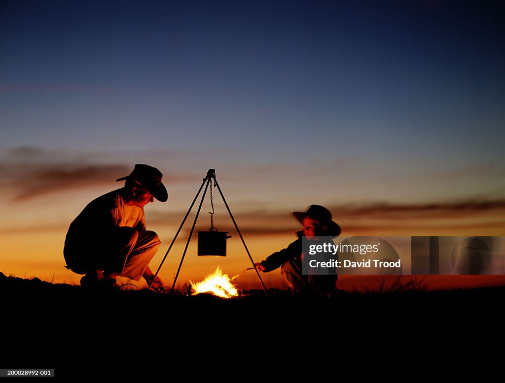 Father and son (4-6) cooking on camp fire