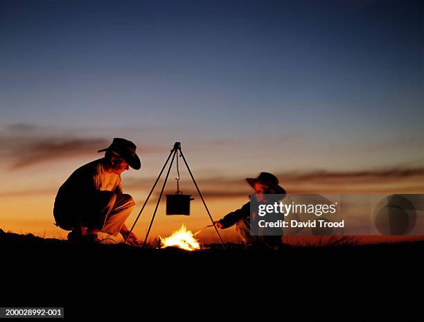father and son (4-6) cooking on camp fire - australia fire - fotografias e filmes do acervo