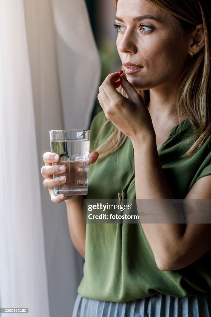 Woman standing by the window, taking her medication