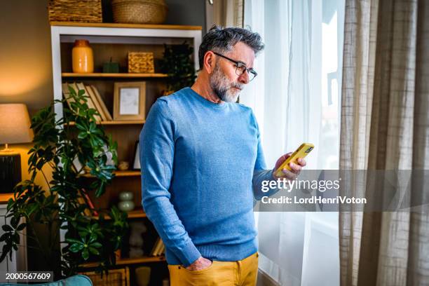 reife mann mit telefon zu hause - websurfen stock-fotos und bilder