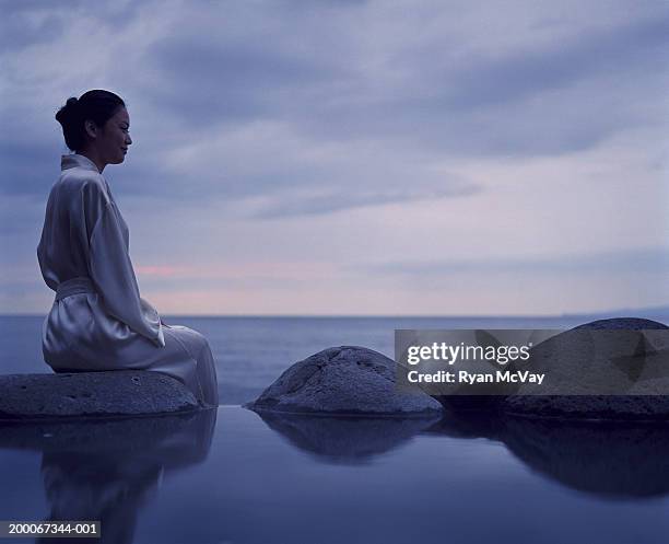 young woman sitting beside hot spring, sea in background - hot spring 個照片及圖片檔