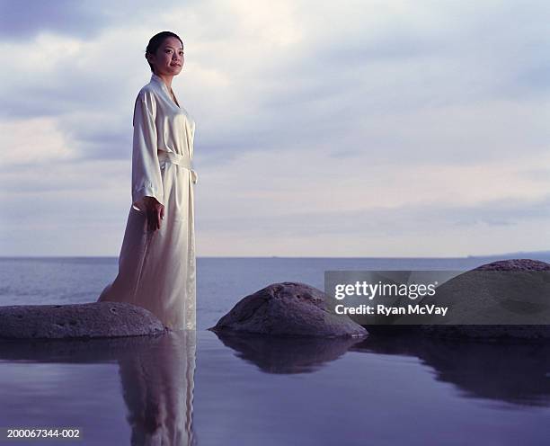 young woman standing beside hot spring, sea in background - robe stock pictures, royalty-free photos & images