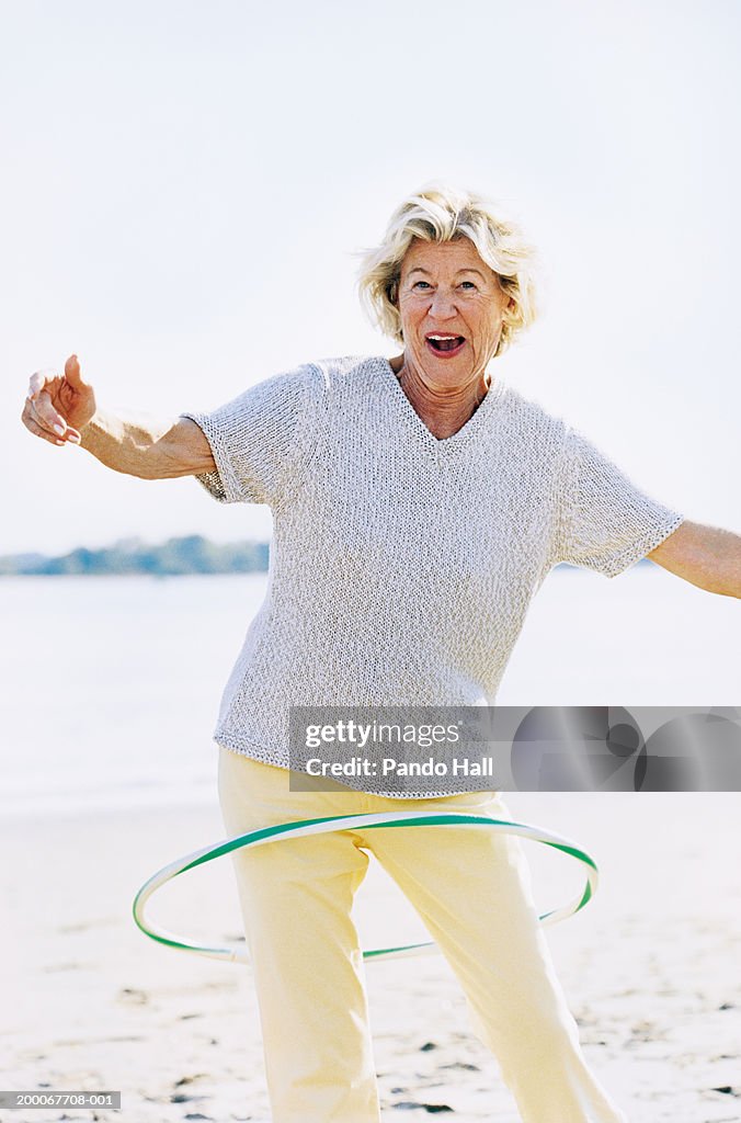 Mature woman spinning plastic hoop around body on beach, portrait