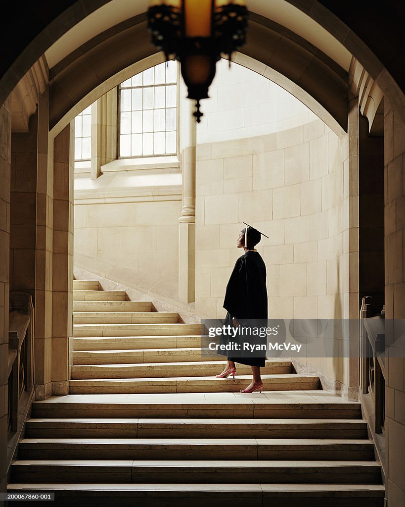 Women wearing graduation cap and gown, ascending staircase, rear view