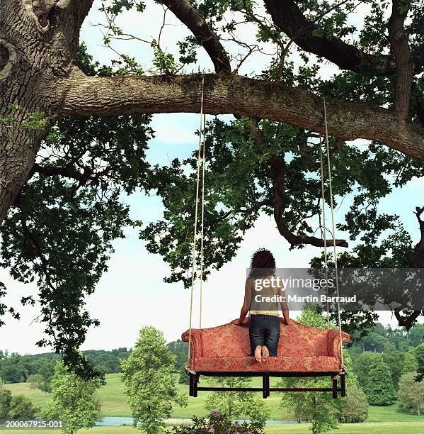 young woman kneeling on sofa strung from tree, rear view - alleen jonge vrouwen stockfoto's en -beelden