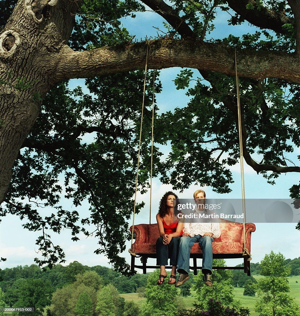 Young couple side by side on sofa strung from tree, portrait of man