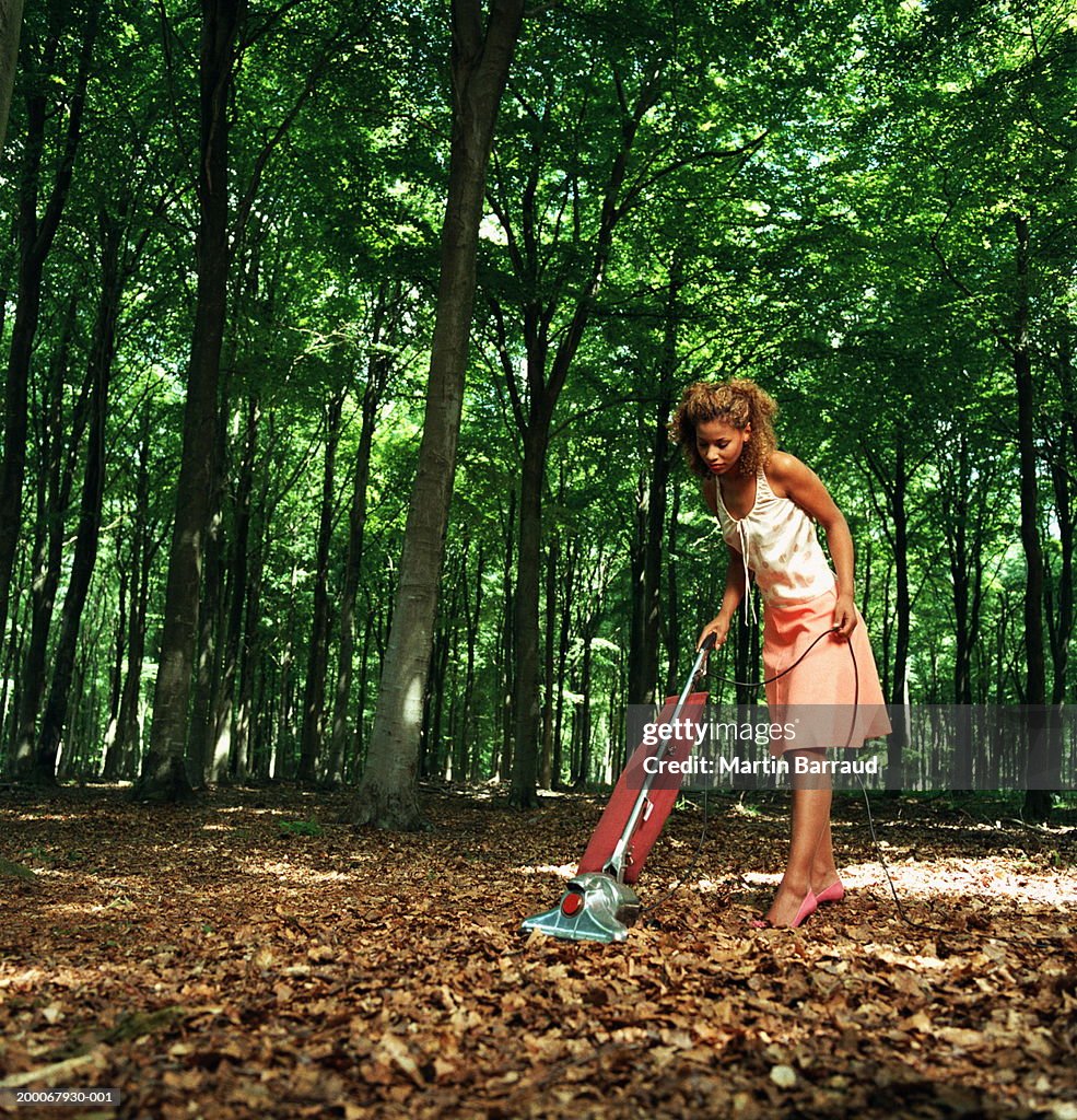 Young woman vacuuming fallen leaves on forest floor