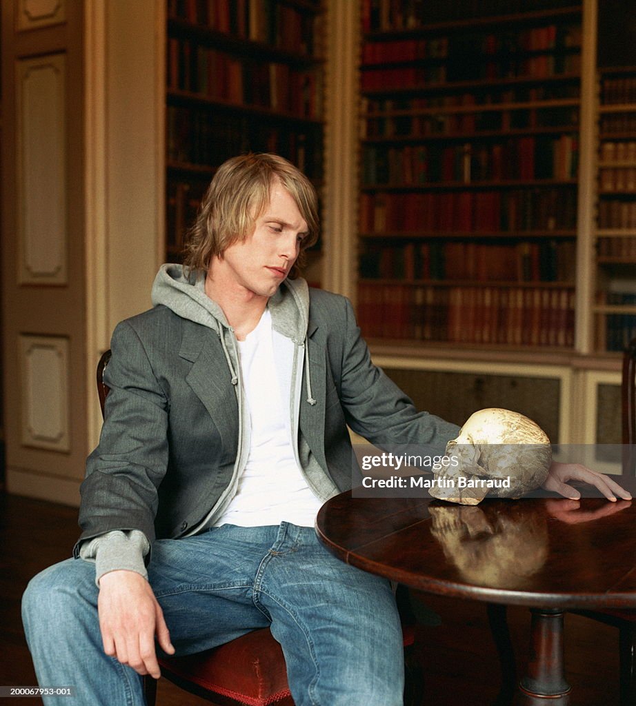 Young man at table staring at skull