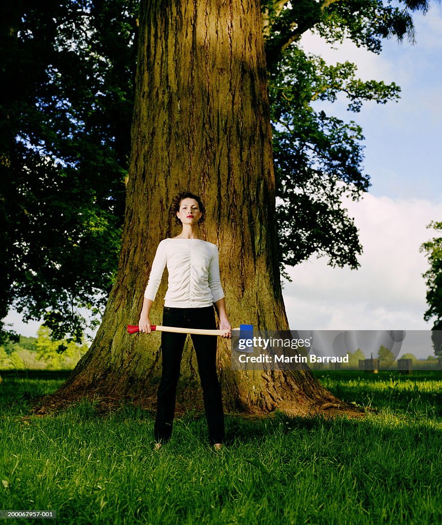 Young woman at foot of tree holding axe, portrait